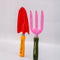side view of set of two metal gardening tools: red and yellow 'plant parent' towel and pink and green 'plant parent' trident