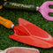 up close of two metal gardening tools: red and yellow 'plant parent' towel and pink and green 'plant parent' trident