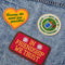 set of 3 embroidered patch stickers: yellow heart with green 'having the most fun possible' across the front, white round 'most likely to glue my fingers together' and red rectangular 'in friendship we trust' on a jean jacket