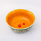 top view of green small ceramic serving bowl with orange interior and red strawberry stamp inside and light blue trim