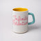 yellow interior of ceramic mug with paper lines and pink cursive 'infinite potenial' typography across the front and light blue handle
