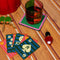 low ball glass set with four colors sections: pink, green, orange and red on a beaded coaster with playing cards near