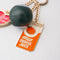 up close of fidget keychain with gold heart photo frame, enamel orange juice charm, and 8-ball de-stress ball