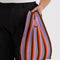 model holding lavender, orange and black vertical stripe pleated baggu