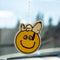 snoopy laying on a yellow smiley face air freshener hanging from a mirror