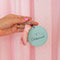 model holding light blue leatherette mirror keychain with cursive 'delusional' across the front and with heart and ballet slipper charm