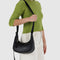 model carrying small black recycled leather crescent bag with monochromatic strap