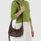 model carrying small brown recycled leather crescent bag with monochromatic strap