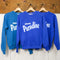 blue sweatshirt with white 'GREETING FROM...PARADISE' across the front hanging on a hanger
