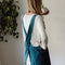 back view of model wearing peacock blue cotton apron with large front pocket and criss-cross back