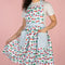model wearing blue gingham cherry print cotton apron with blue grid patch pockets and straps