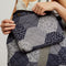 model holding blue, black and grey quilted patchwork bag with matching zip pouch