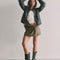 model wearing olive green mini skirt with pleated front and raw hem