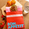 pink and coral snack bag with light blue 'bon appetit' across the front on a table