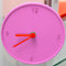 pink round clock with red hands on a shelf