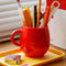 red melamine mug with pens and pencils inside