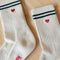 up close of white high screw socks with red and blue stripes on the top and red embroidered heart