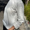 side view of model wearing relaxed fit white long sleeve top with slight distressing around the collar