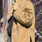 side view of model wearing relaxed fit brown/tan waxed cotton jacket with side pockets, high collar and side vents