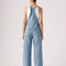 back view of model wearing light denim relaxed fit overalls with front pockets