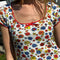 up close of model wearing white cotton mini dress with red lettuce trim, bow on the front bust, and retro primary color floral print