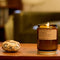 arroyo oak standard candle in a amber colored jar and gold twist lid burning on a table