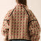 back view of model wearing tan fleece half zip sweatshirt with red floral print and black piping on the arms and zipper