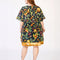 back view of model wearing navy blue babydoll dress with pin-tucked and large white button down the bust, with colorful fruit, baguette and leafy print