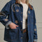 up close of model wearing denim oversized jacket with corduroy collar, patch pockets, and embroidered star, moon and sun pattern