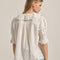 back view of model wearing ivory blouse with embroidered collar and hem, button front and pin-tucked details