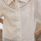 up close of model wearing opened white lace trim button down short sleeve blouse with all over embroidered and inlets