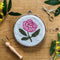 completed pink peony needlepoint kit surrounded by greenery