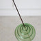 green stacked glass incense holder with an incense inside on a table
