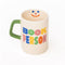 cream ceramic coffee mug with green handle and colorful 'book person' across the front and smiley face inside
