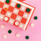 Double-sided pink and red checkers and backgammon board with green and cream wood pieces and built-in storage drawer.