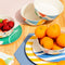 editorial image of cream set of bamboo bowls with colorful abstract flora print, plates, and vibrant fruit