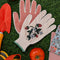 cream gardening gloves with white flower and strawberry print and green trim in the grass surrounded by gardening tools
