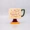 cream short ceramic mug with pink cursive 'in my growing season' with green handle and pink and yellow pedestal 