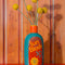 teal ceramic vase with red and yellow 'sunblock 30 SPF' label and yellow flowers inside on a red table