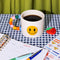white ceramic mug with rainbow shapes handle and yellow smiley face on the front on a green and navy gingham background