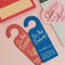 blue bookmark in the shape of a door hanger with white 'do not disturb!i'm currently lost in a fantasy world and i don't want to leave!' across the front on a pink ground