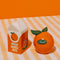 orange shaped and orange juice carton salt and pepper shakers on a table with a striped tablecloth