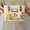 model holding cream metal seed box with floral and butterfly print on the bottom and three interior compartments