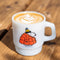 white mug with snoopy in a large red puffer jacket and yellow beanie with a latte inside