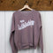 rosewood sweatshirt with white Bonjour De La Bibliothèque across the front hanging on a hanger