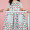 model showing adjustable strap waist of blue gingham cherry print cotton apron with blue grid patch pockets and straps