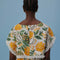 back view of model wearing white crop top with fringe detail and mixed fruit print