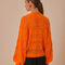 back view of model wearing orange open knit textured cardigan with slight puff sleeves and fashion button front
