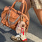 model carrying brown leather barrel purse with long strap zipper pulls and various zipper compartments