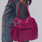 model carrying raspberry pink leather tote bag with several zipper pockets, double handles, and crossbody strap